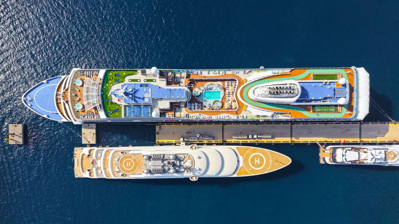 our-story Top-down view of two luxurious cruise ships moored at a sunny port, showcasing pools and helipads.